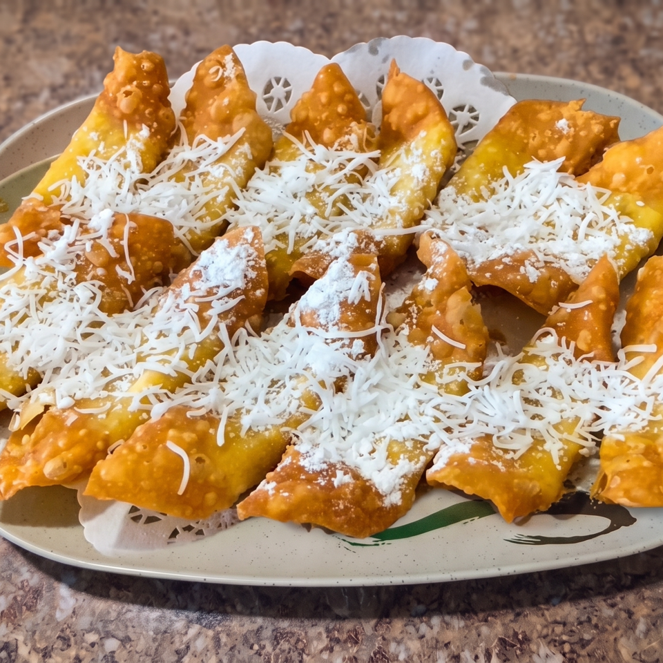 Plate of golden fried pastries topped with shredded white cheese and powdered sugar on a decorative liner.